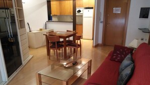 Un espacio habitable compacto con comedor, kitchenette y un sofá rojo con cojines.