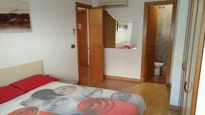Un dormitorio con cama, almohada roja, armario de madera y baño visible a través de una puerta abierta.