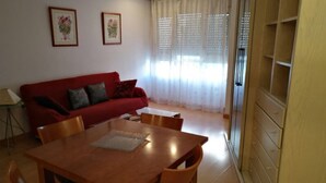 Un comedor con mesa y sillas de madera, un sofá rojo y una ventana con cortinas translúcidas.