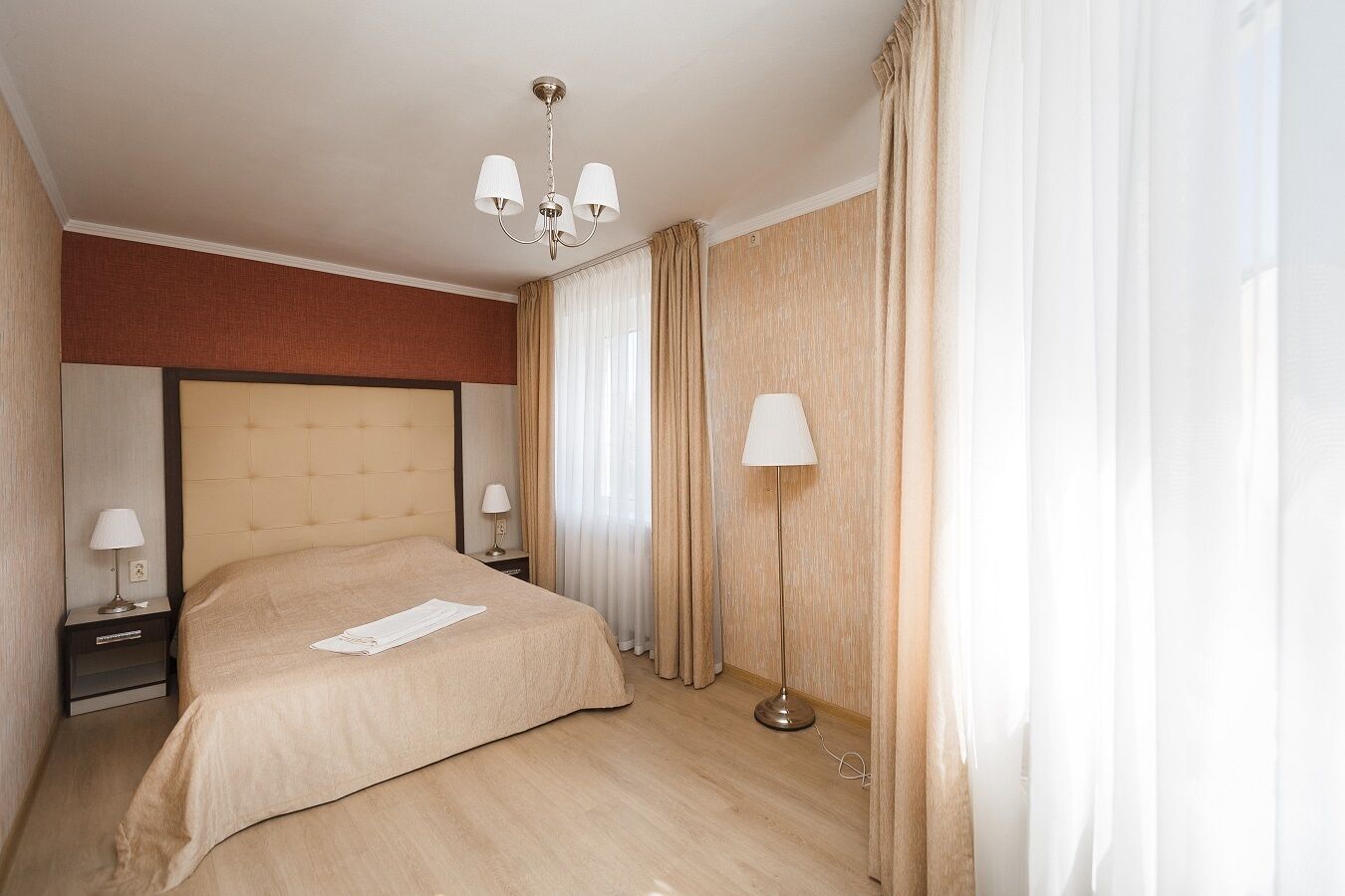 A hotel room with a large bed, two bedside tables with lamps, a floor lamp, and a chandelier.