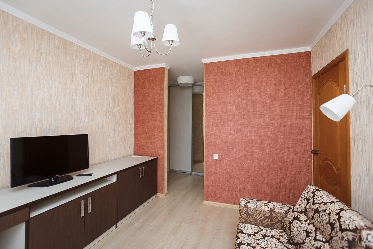 A modern living room with a flat-screen TV, dark wooden cabinets, a patterned sofa, and a hallway with red textured walls.