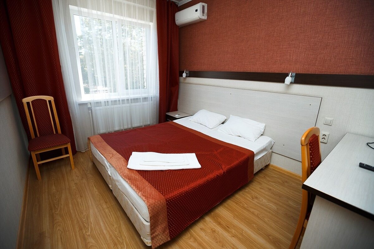 A hotel room with a bed, a chair, a desk, and a window with curtains.