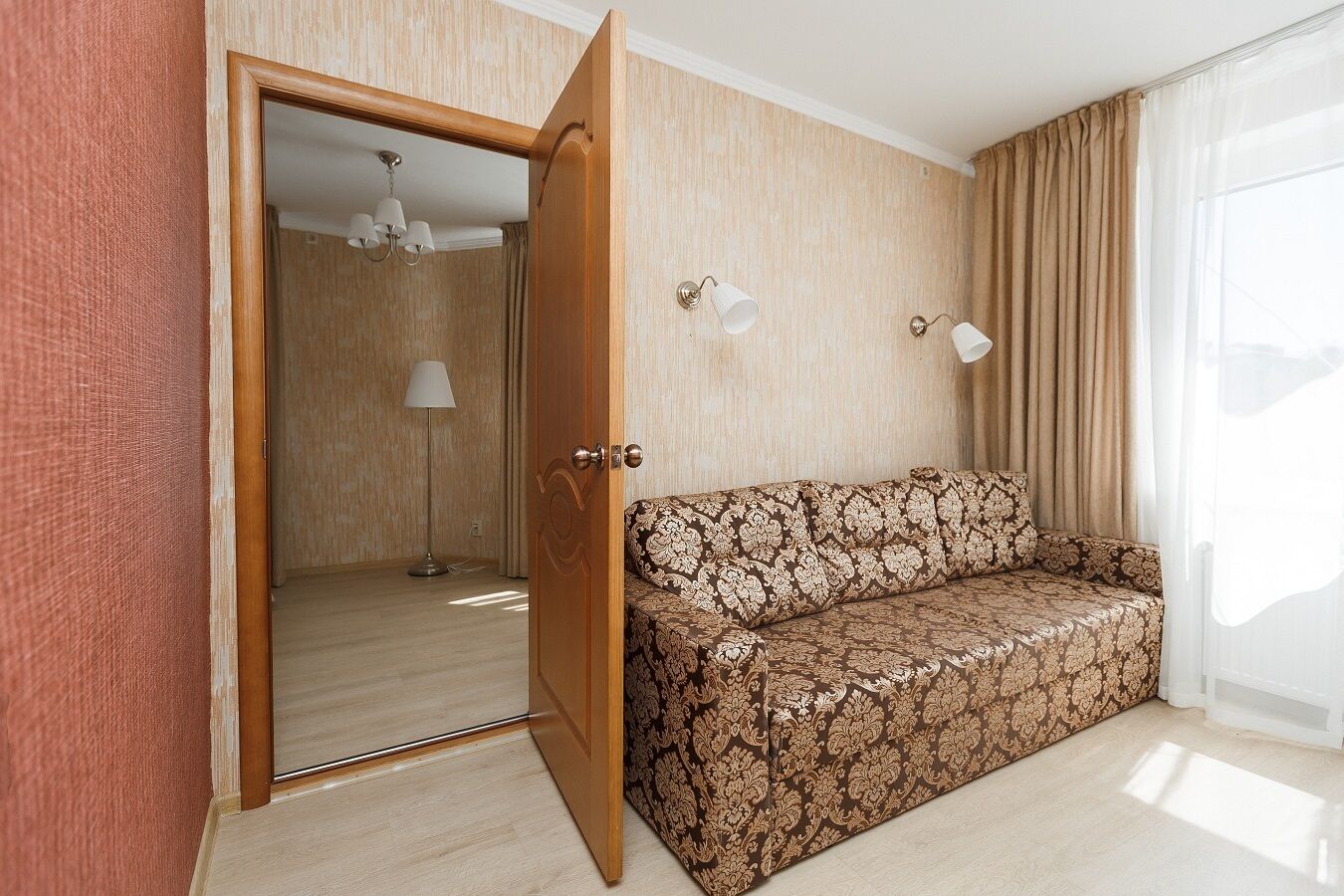 A room with a patterned sofa, a wooden door, a lamp, and a ceiling light.