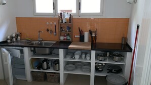 Una cocina con pileta, estufa y estanterías con vajilla y utensilios de cocina.