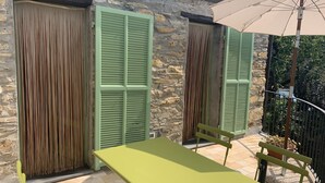 Un edificio de piedra con contraventanas verdes, una mesa y sillas en un patio empedrado.