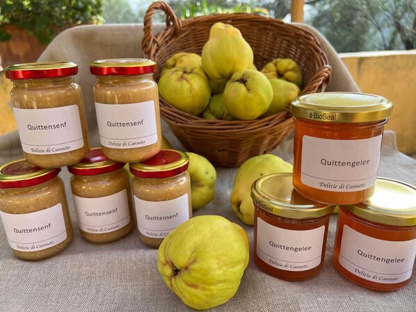 Varios frascos de Quittensenzf y mermelada de Quittengelee, una cesta de peras y una sola pera frente a los frascos.
