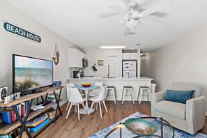 Un espace de vie compact comprenant un coin repas, une kitchenette et un téléviseur diffusant une scène de plage.