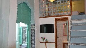 A room with a television mounted on the wall, a small table with a vase of flowers, and a decorative metal screen. - Riad Louane (Rabat)