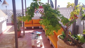 A covered outdoor seating area with a wooden pergola, orange cushions, and potted plants. - Riad Louane (Rabat)