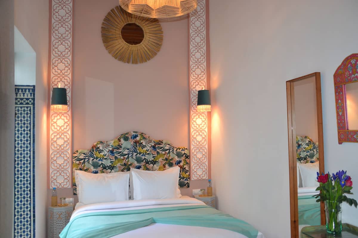 A bedroom with a bed, decorative wall panels, a mirror, and a vase with flowers.