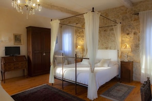 A bedroom with a four-poster bed, a chandelier, a television, and a stone wall.