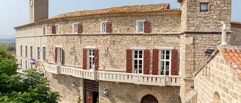 A stone building with a balcony, multiple windows, and a flag.