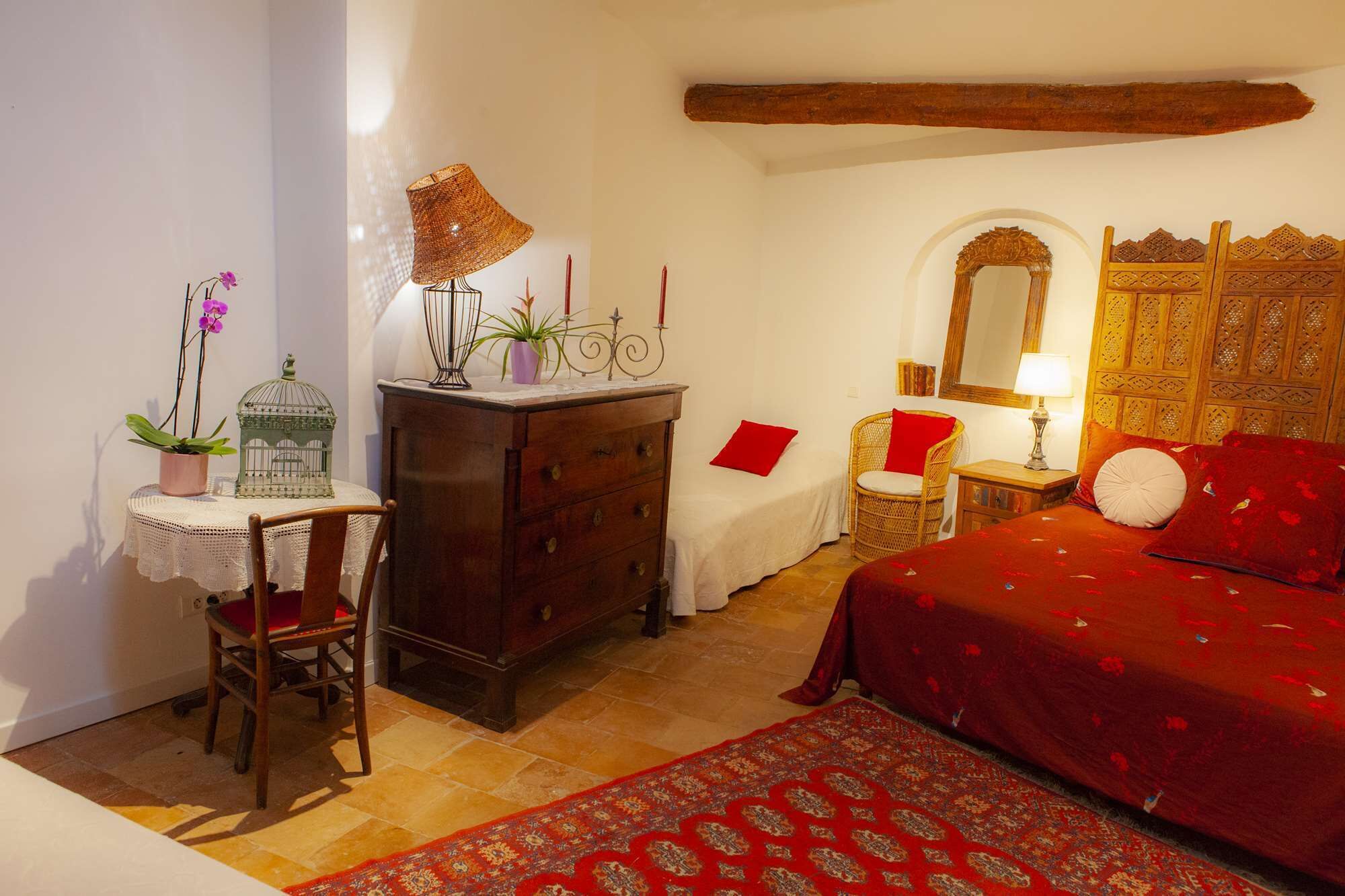 Un dormitorio con cama, cómoda, silla, mesa, lámpara, espejo y una pequeña planta en maceta.