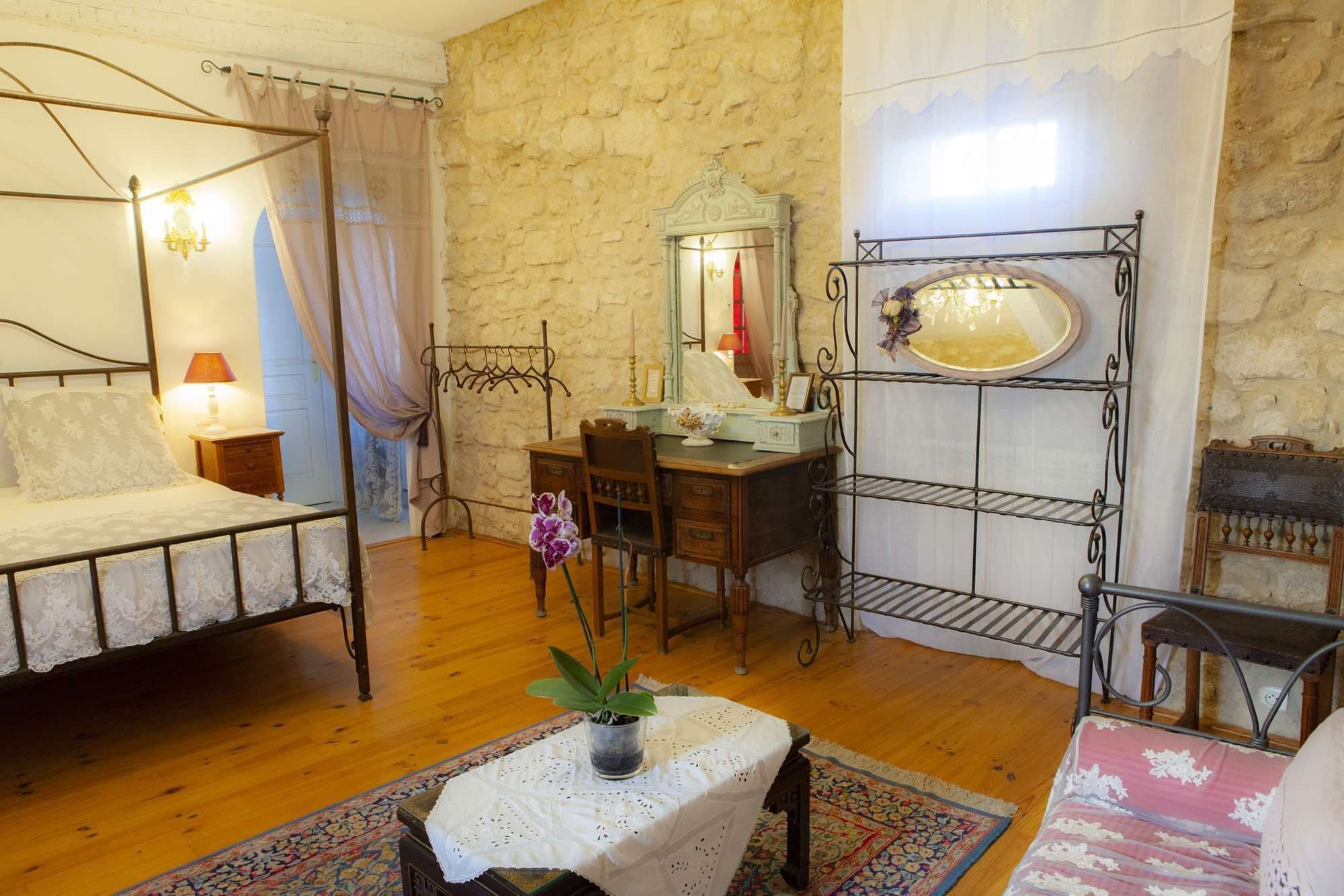 Ein Schlafzimmer mit einem Himmelbett, einem Holztisch, einem Spiegel und einem kleinen Regal.