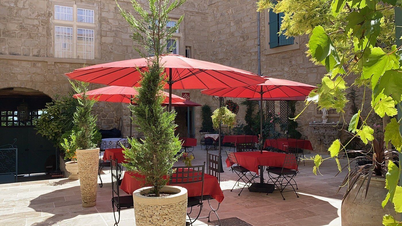 Un espace café en plein air avec des parasols rouges, des tables et des chaises en pierre.