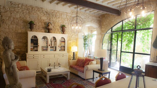 A cozy room with a stone wall, a white cabinet with books, a sofa, a coffee table, and a large window with a view of greenery.