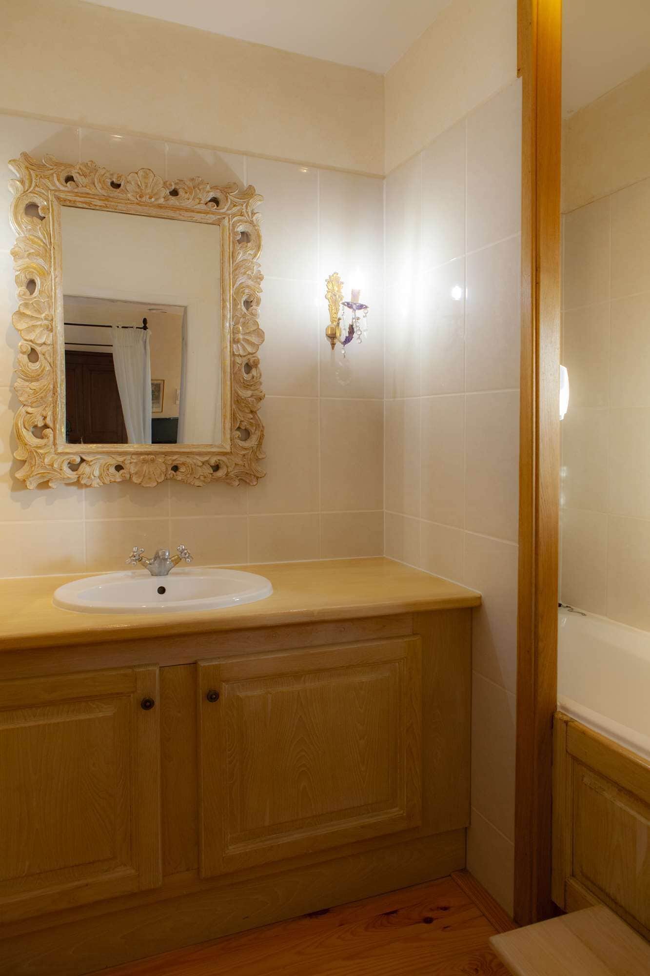 Un baño con tocador de madera, un lavabo blanco y un espejo grande y ornamentado.