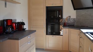 Cocina compacta con armarios de madera, horno Bosch, microondas y televisor de pantalla plana montado en la pared.