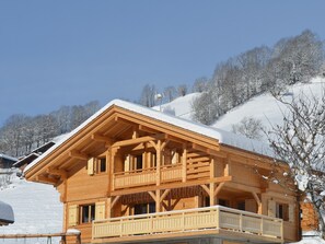 Un chalet en bois doté d’un balcon, situé au pied d’une montagne enneigée.