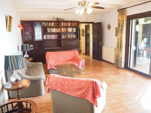 Un salón con dos sofás, una estantería, un ventilador de techo y vistas a través de un ventanal.