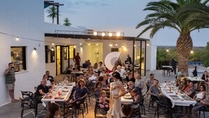 An outdoor dining area with tables and chairs, a stage with a fan, and palm trees. - --- Wood Mobile Home 1 (Calig/Castellon)