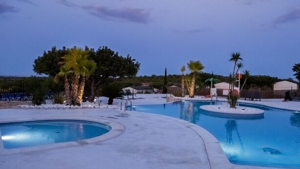 A swimming pool area with multiple pools, palm trees, and a clear sky. - --- Wood Mobile Home 1 (Calig/Castellon)