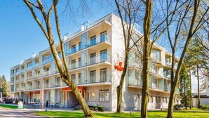 Een modern meerlaags hotel met balkons, een restaurant op de begane grond en een verzorgd gazon.