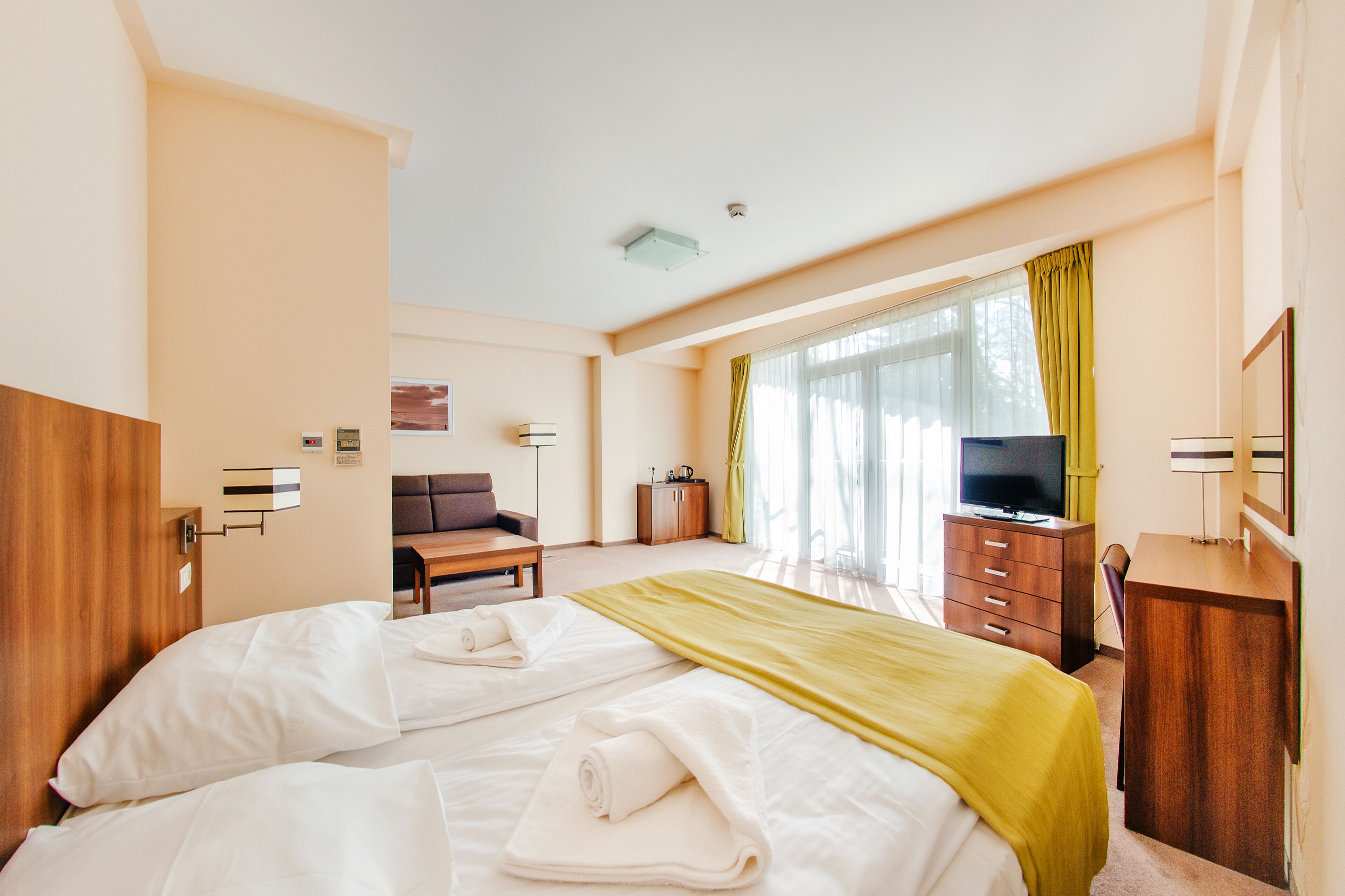 Una habitación de hotel con una cama grande, un escritorio de madera, un televisor y una ventana con cortinas.