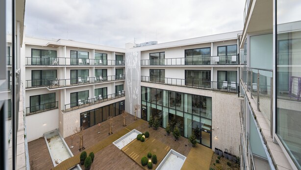 Een modern meerlaags gebouw met balkons, grote ramen en een binnentuin met potplanten.
