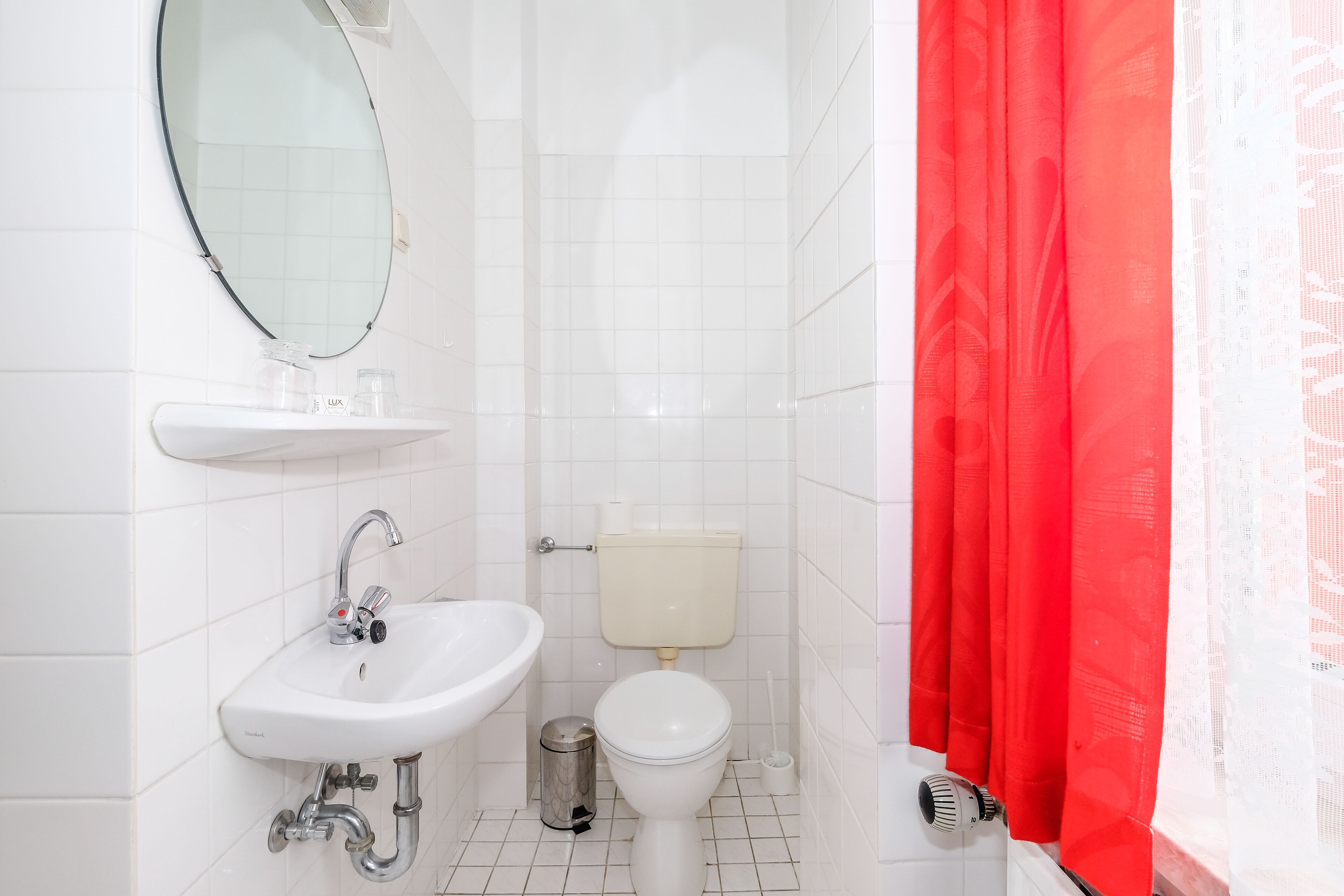 A bathroom with a white sink, mirror, toilet, and red curtains.