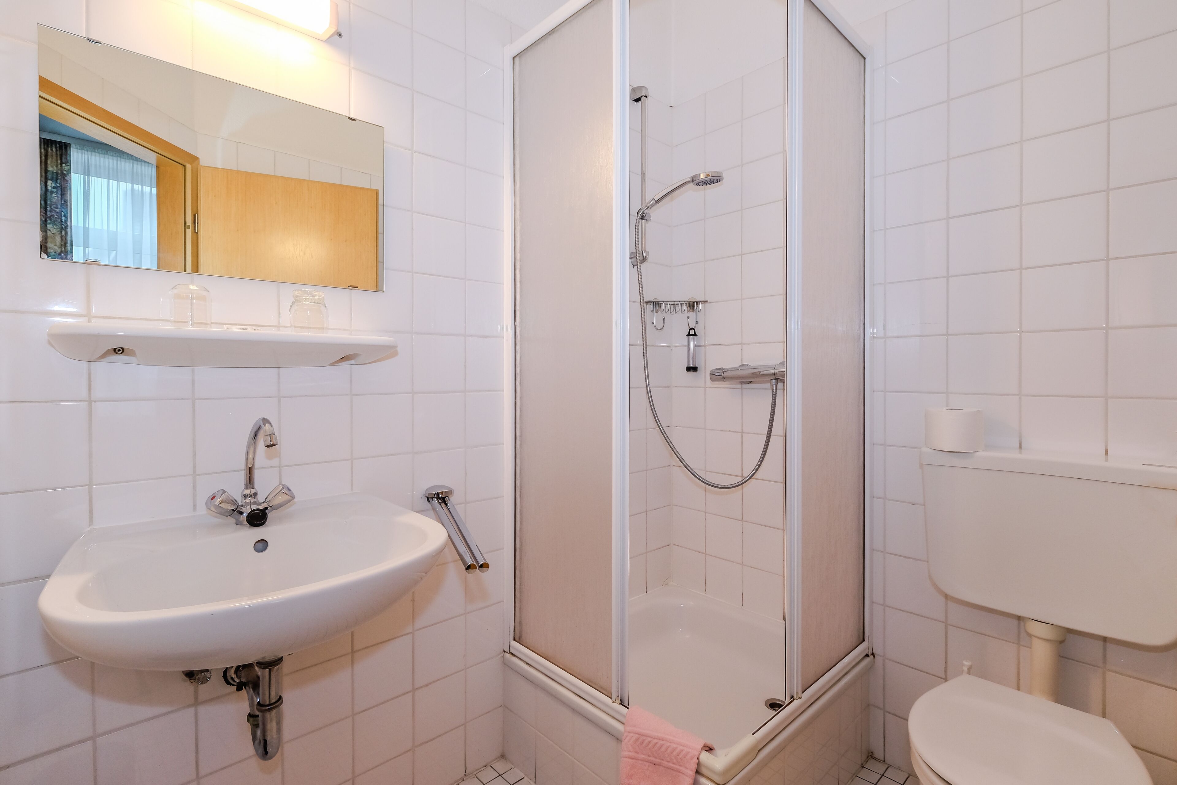 Un baño con lavamanos blanco, espejo, ducha e inodoro.
