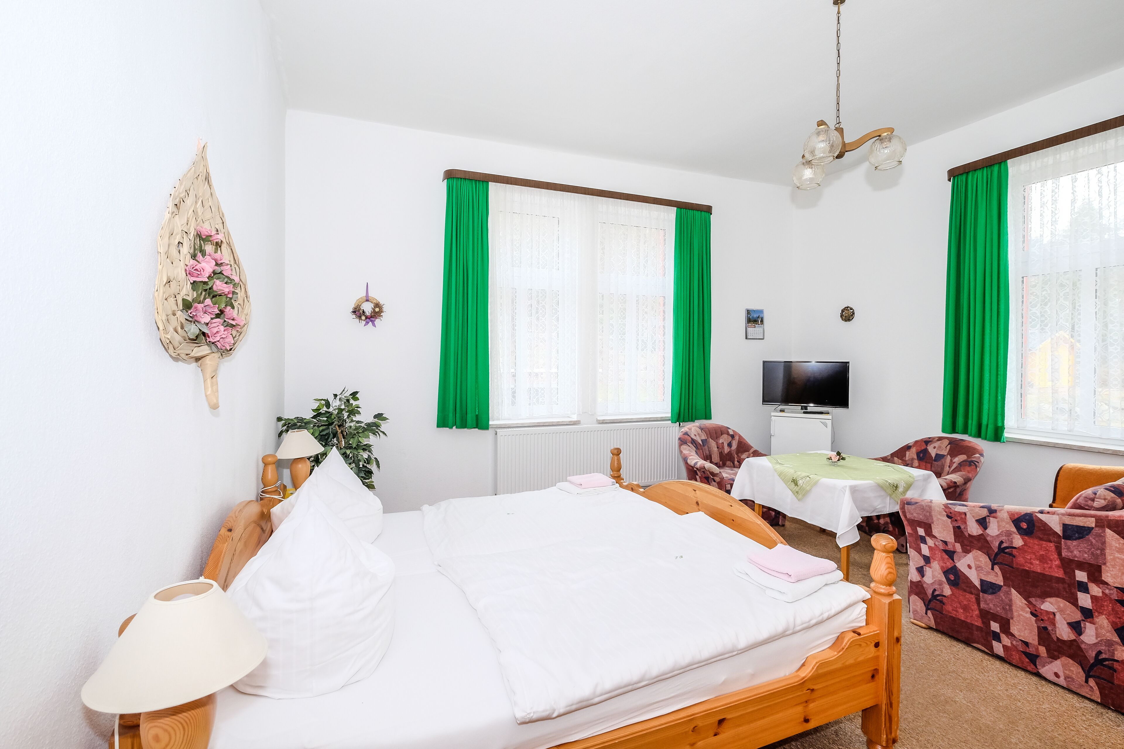 A bedroom with a bed, bedside table, lamp, TV, and a patterned chair.