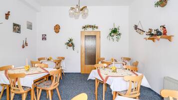 A dining area with wooden chairs and tables, a chandelier, and wall decorations including pictures and plants.