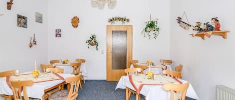 A dining area with wooden chairs and tables, a chandelier, and wall decorations including pictures and plants.