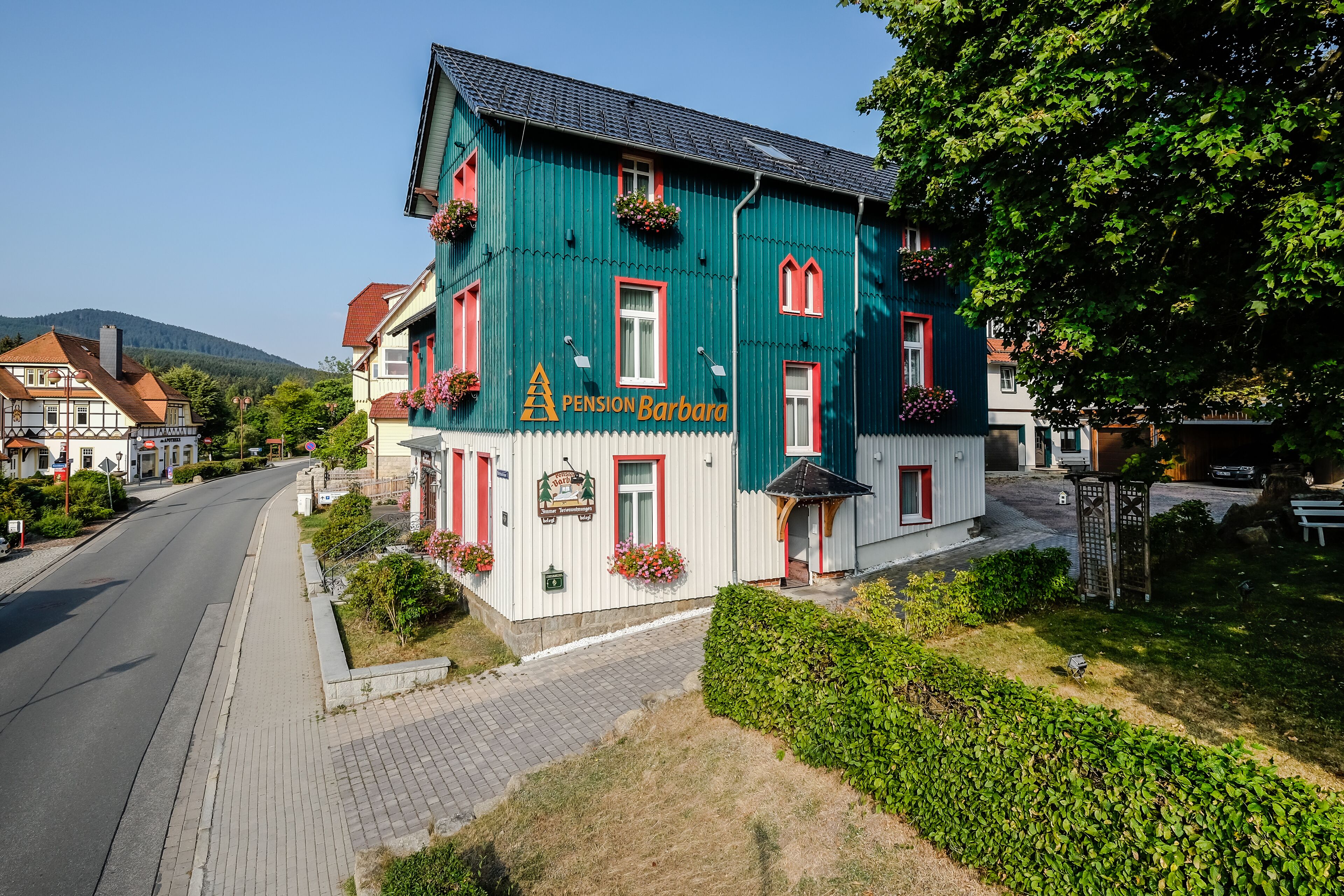 A two-story building with a green facade, red window frames, and flower boxes.