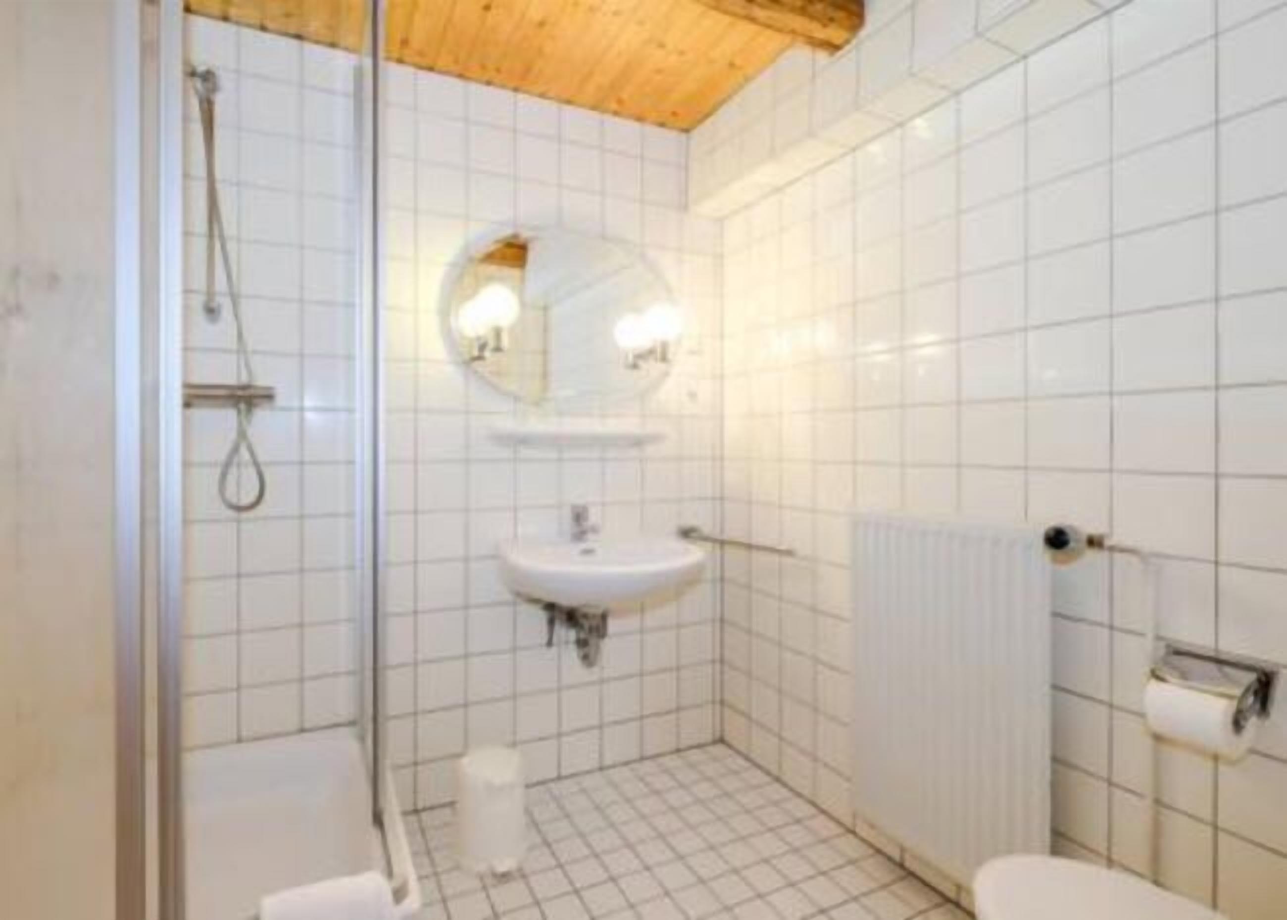 A small, tiled bathroom with a shower, sink, and toilet.