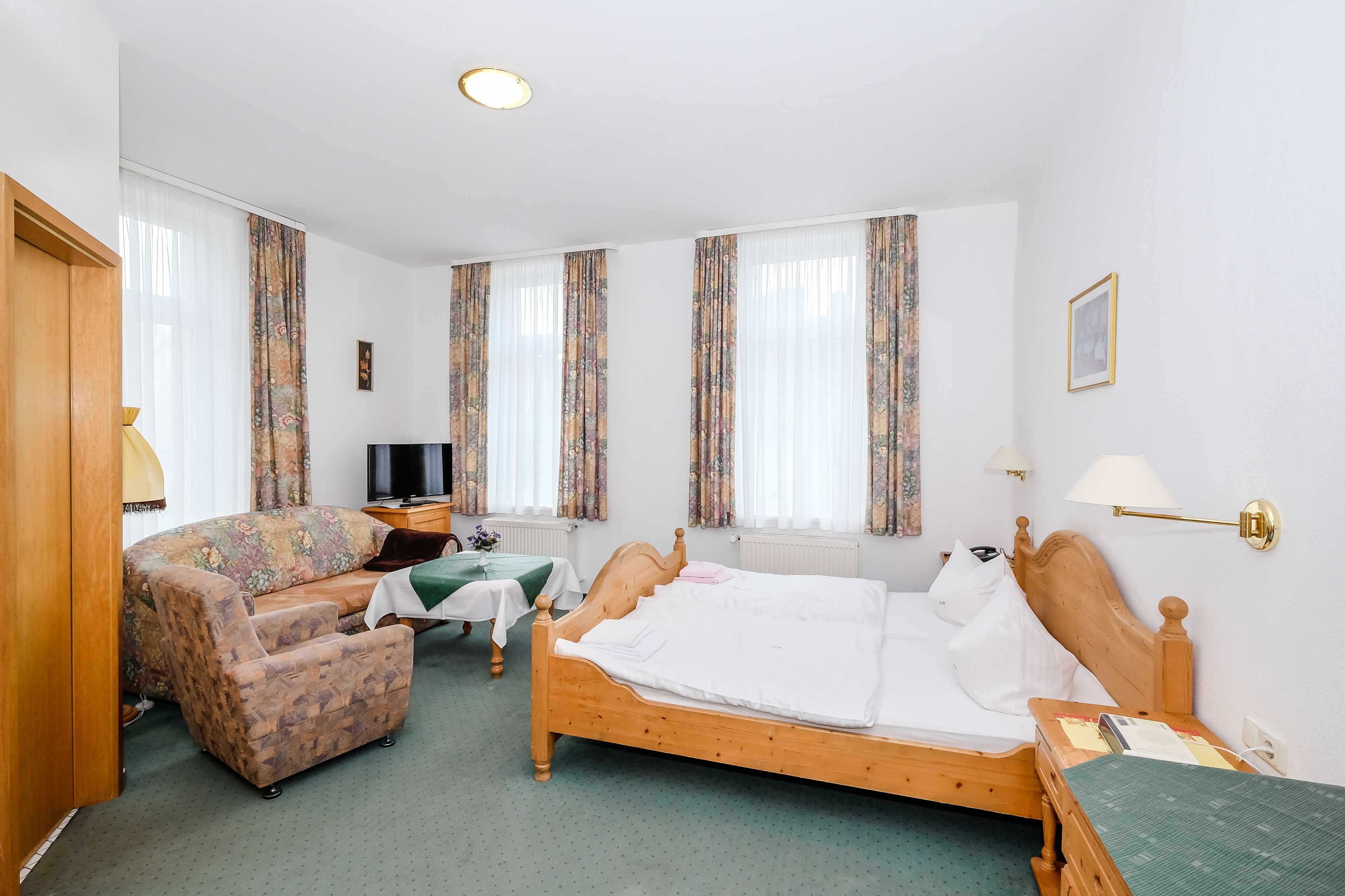 Ein Hotelzimmer mit einem hölzernen Bett, einem grünen Sofa, einem Fernseher und einem kleinen Tisch.