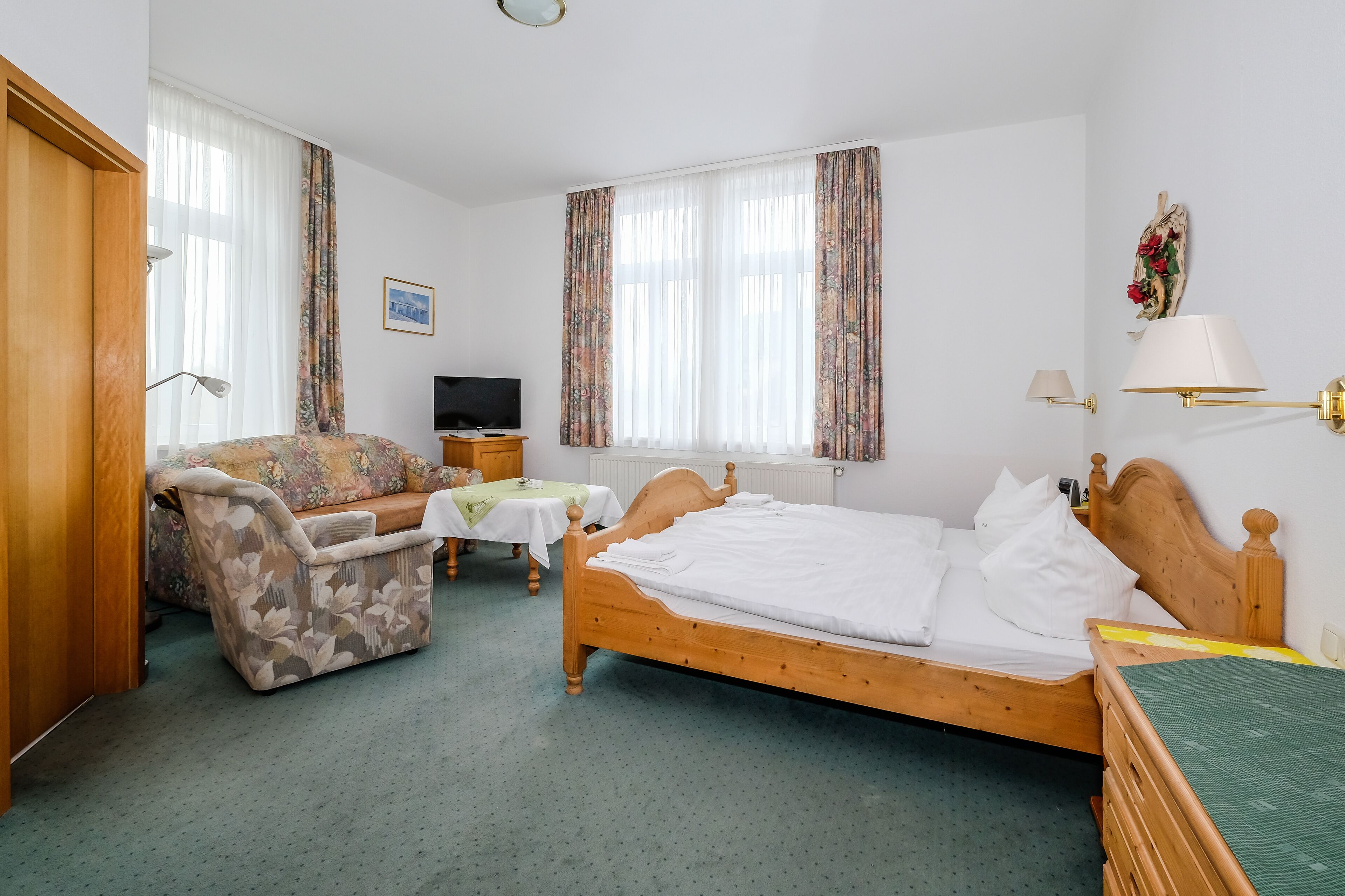 A hotel room with a wooden bed, a sofa, a TV, and a desk with a lamp.