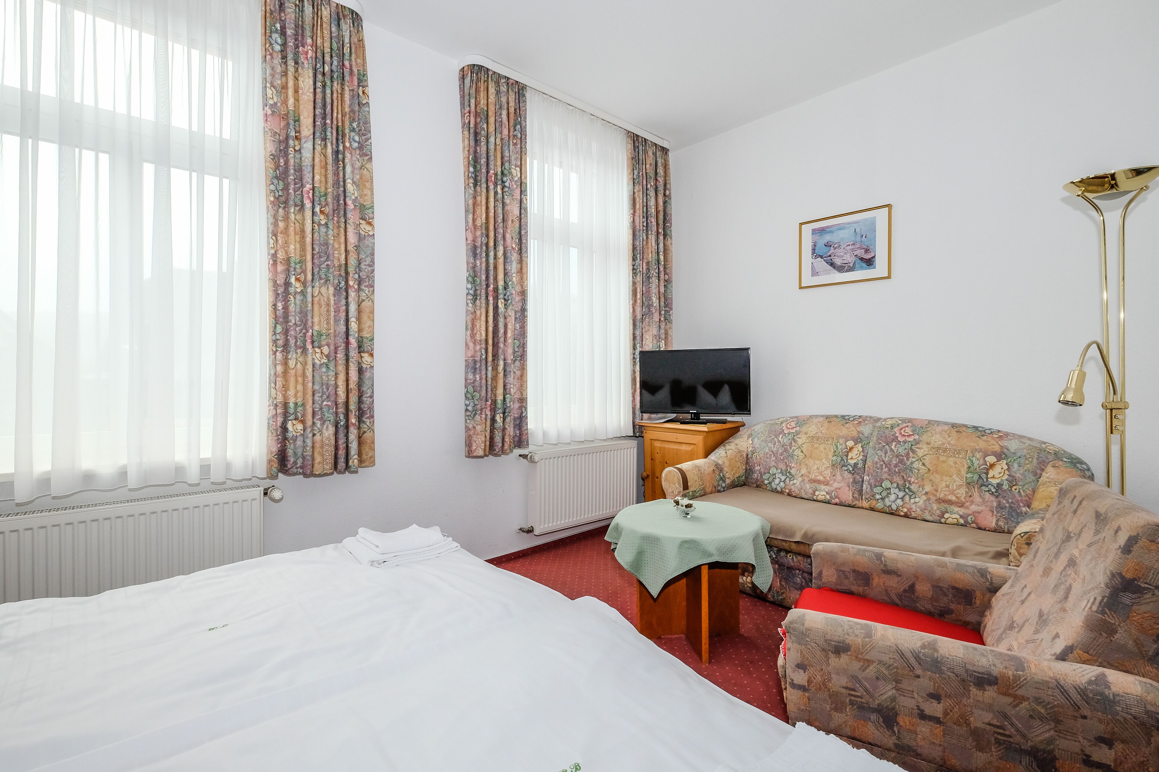 Una habitación de hotel con cama, sofá, televisión, una mesita y una lámpara.