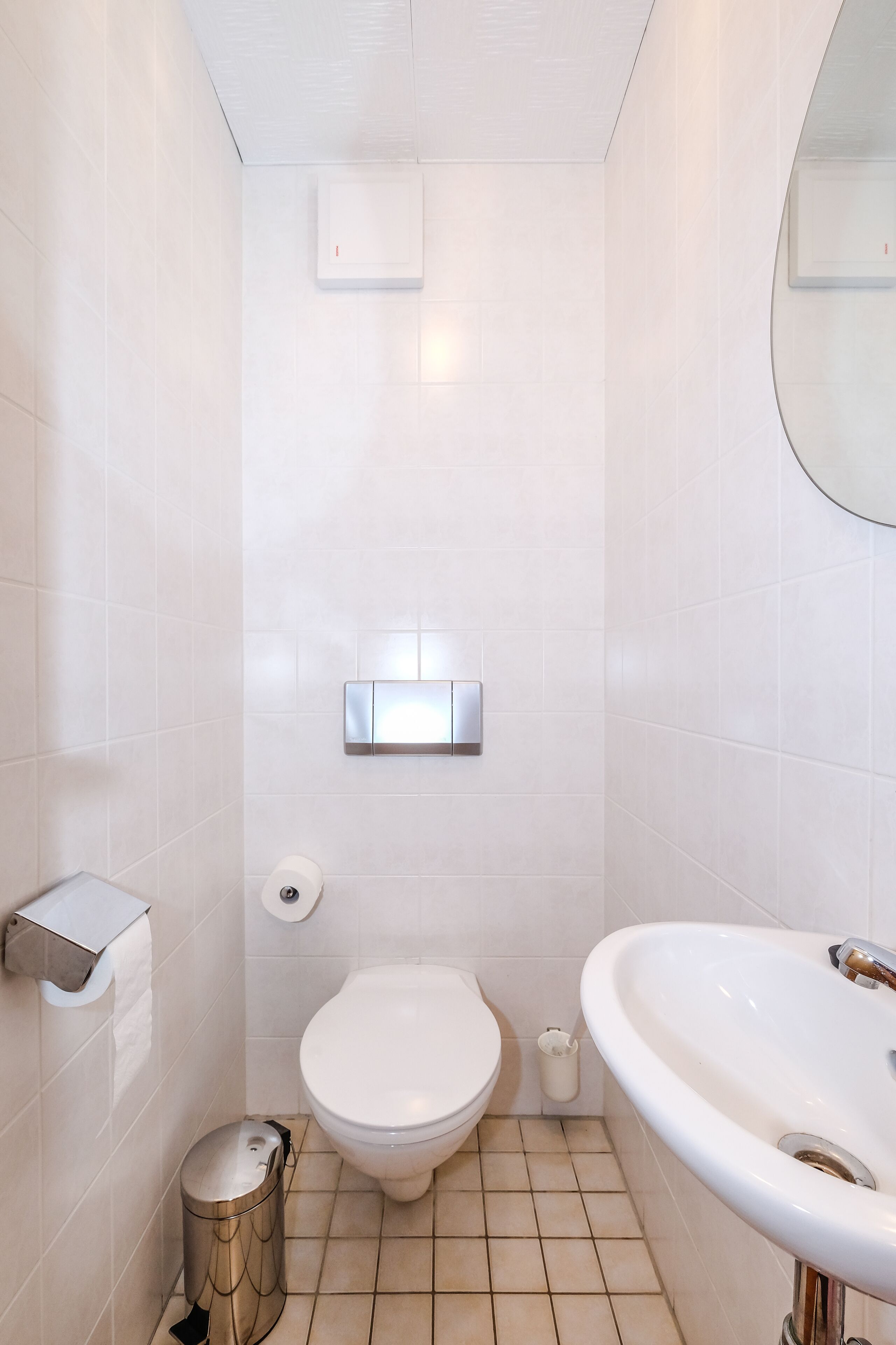 A modern bathroom with a toilet, sink, and trash bin.