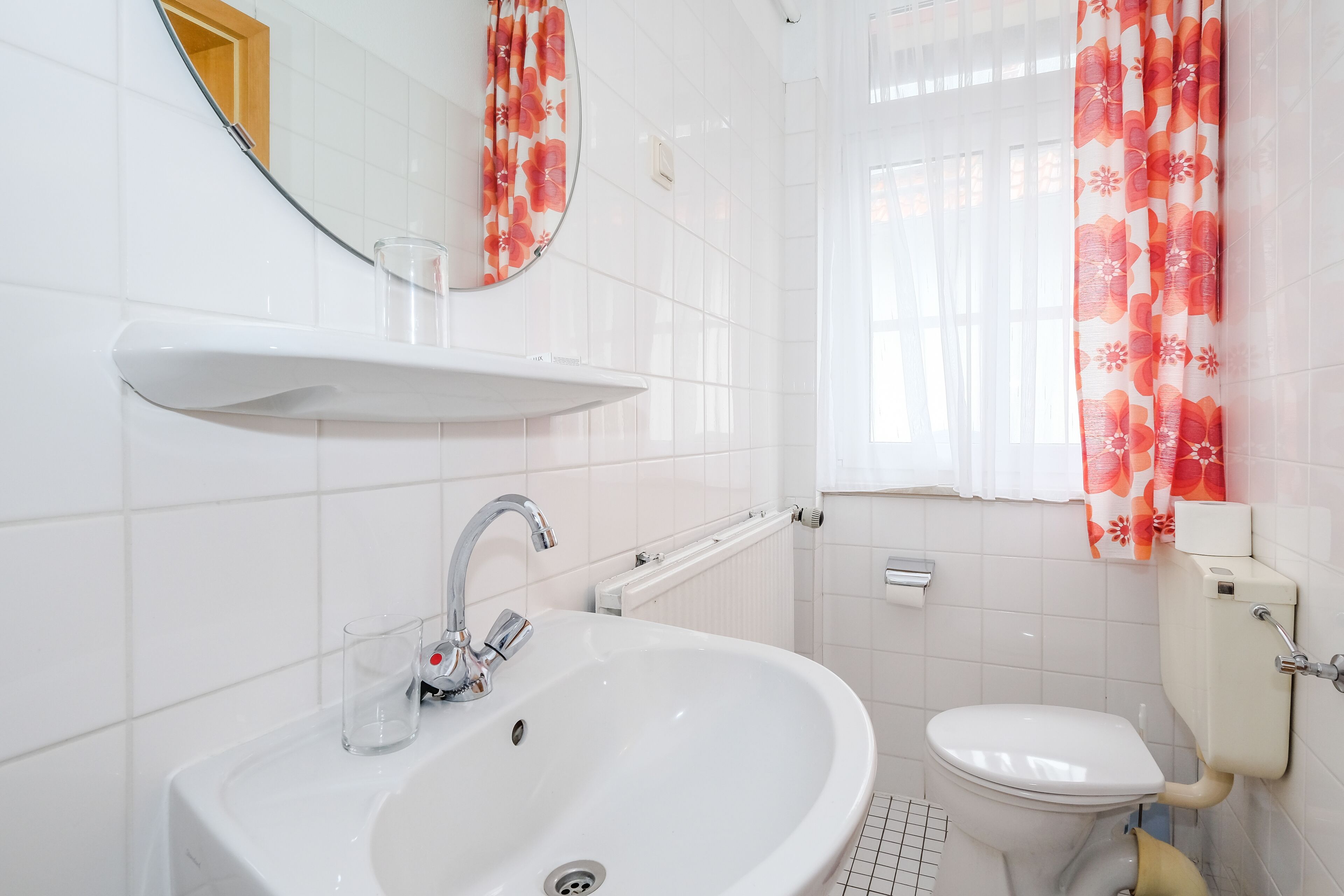 Et badeværelse med en hvid vask, spejl og toilet.
