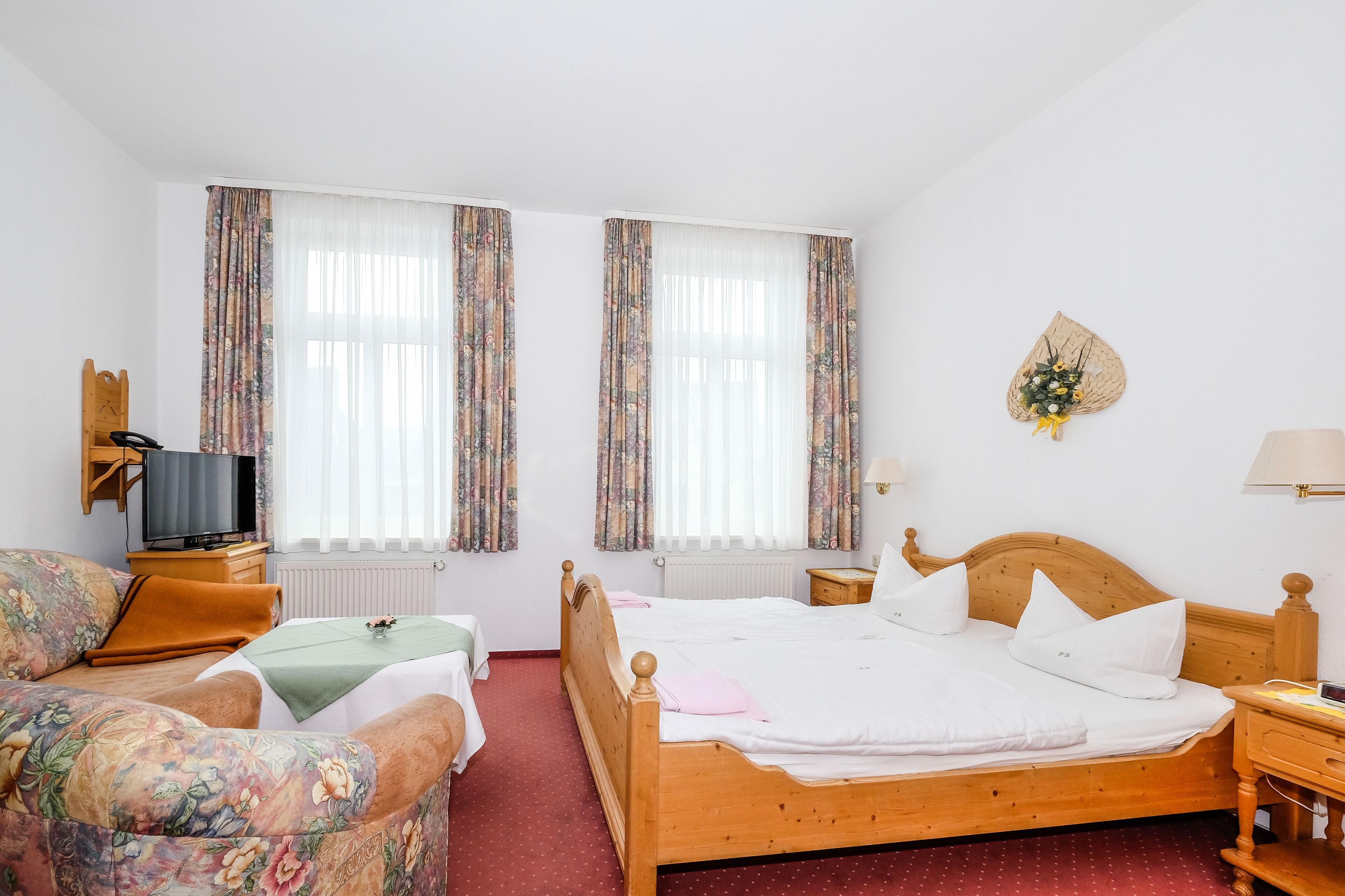 Habitación de hotel con cama de madera, dos mesitas de noche, televisión y cortinas con estampado floral.