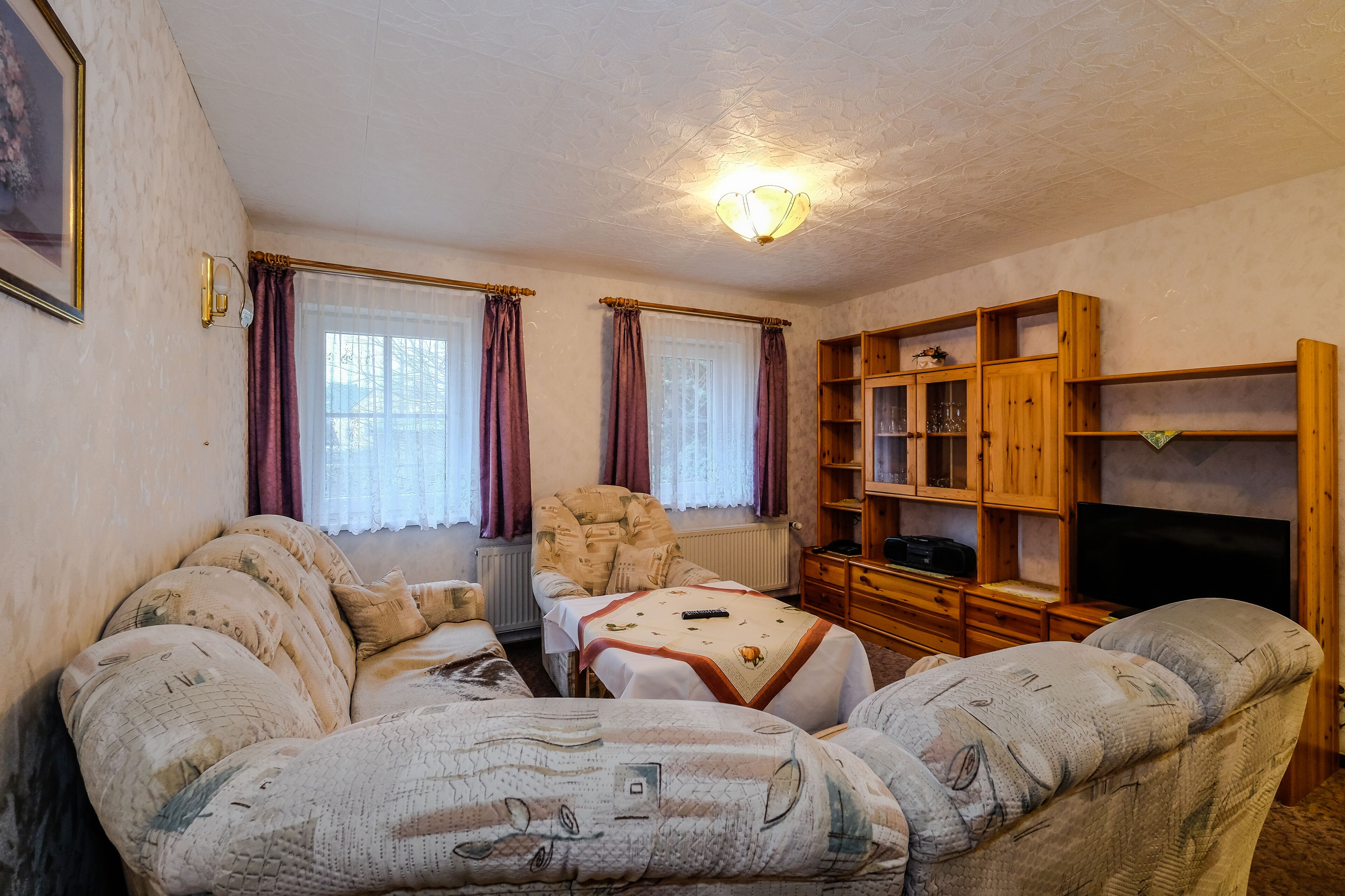 Een gezellige woonkamer met een bank, fauteuil en een houten kast met glazen deuren.