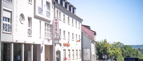 A hotel with a sign reading "HOTEL TANNEN" on a street with parked cars.