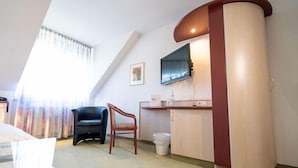 A hotel room with a curved wooden cabinet, a flat-screen TV mounted on the wall, a black leather chair, and a small table.
