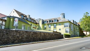 A hotel with a green facade, multiple windows, and a stone wall in front.