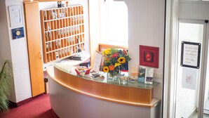 A reception desk with a glass top, a bulletin board, a flower vase, and a red-framed picture on the wall.