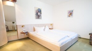 A neatly arranged hotel room with a large bed, bedside tables, a mirror, and artwork on the walls.