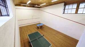 A squash court with a green table, wooden floor, and white walls.