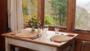 A wooden table set for two with a woven placemat, a vase with flowers, and two wine glasses.